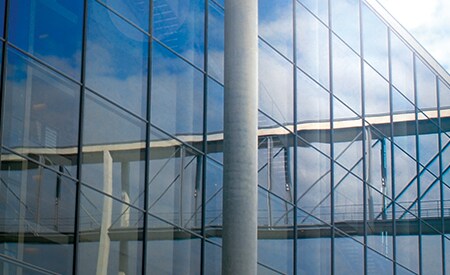 Large window-covered building reflecting blue sky and clouds
