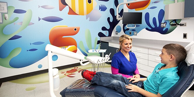 Child in dentist chair and smiling dental technician in dentist’s office with vibrant ocean illustration printed on 3M Graphic Films.
