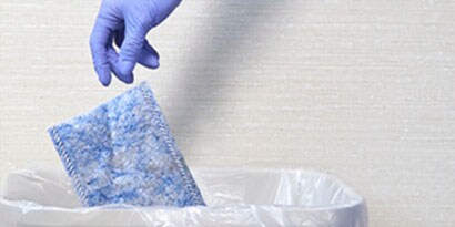 person’s hand with a cleaning glove on, throwing away a disposable mop pad to reduce cross-contamination
