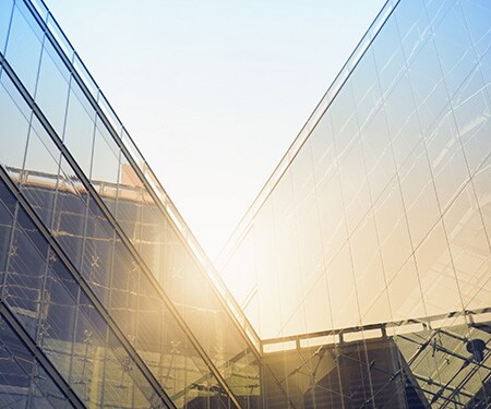 Bright sun shining over angular window-covered buildings
