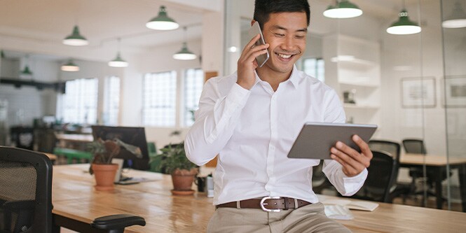 Image of smiling businessman talking on phone and looking at tablet.
