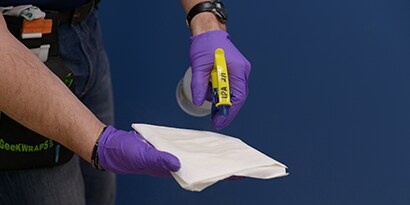 Person with blue surgical gloves spraying a paper towel with 3M enhanced adhesion spray
