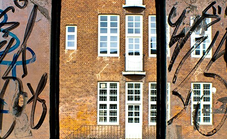 3-paned window looking out on brown brick building. Side panes have black graffiti covering glass, middle pane is clear and clean
