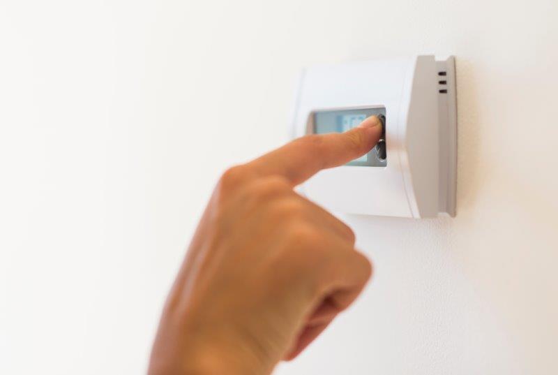 A young woman adjusts the temperature on her thermostat.
