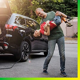 Man playing with son by a black car charging in driveway