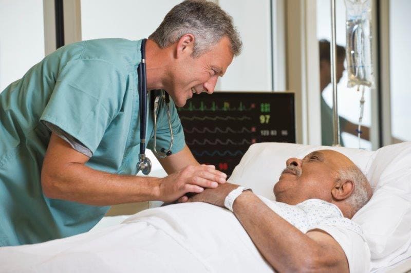 Healing sunlight streams through the window as a female nurse in blue scrubs tends to a patient.

