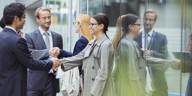 Group of businesspeople greeting each other in front of window covered office building

